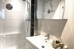 Salle de bain avec une grande douche à l'italienne et un lavabo avec tablette et armoire pour déposer les affaires de toilette